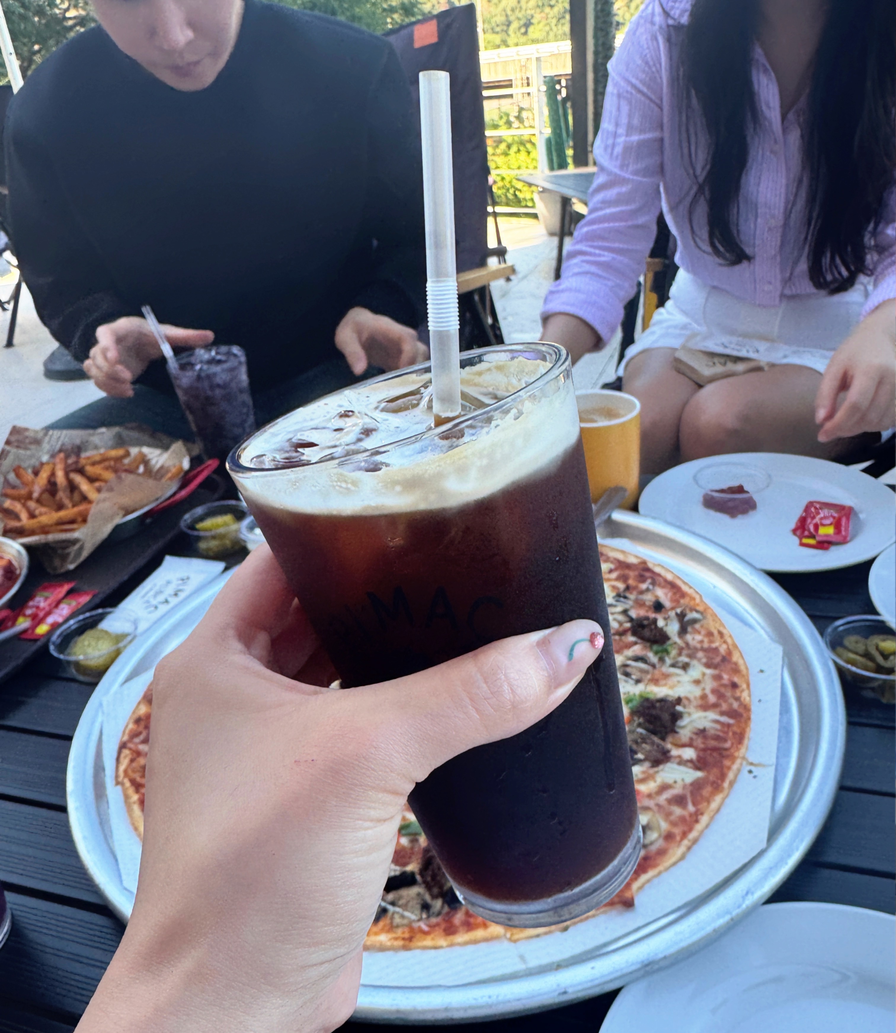 팔당 피맥플레이스 테라스에서 아이스아메리카노를 들고 있는 모습. 테이블 위엔 피자와 감자튀김이 놓여 있다.
