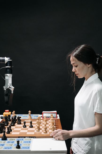 여성이 로봇 팔과 함께 전략적인 체스 게임에 참여하여 AI 혁신을 강조합니다.