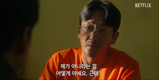 강인구가 죄수복을 입은 채로 앞에 있는 사람을 응시하고 있다.