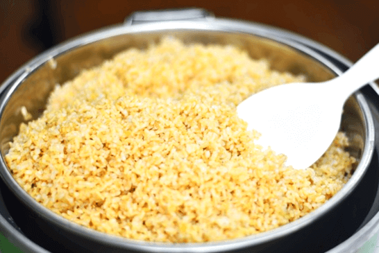 은색 남비에 갈색의 현미밥이 한가득 있다. 밥 오른쪽에는 하얀 밥자가 있다.