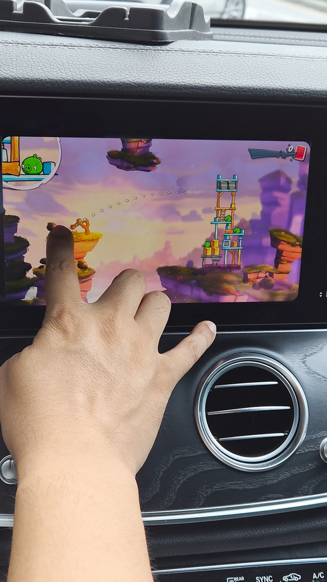 차량 디스플레이에 앵그리버드2 실행 중&amp;#44; 손가락으로 화면을 터치해 슬링샷을 조준하는 장면