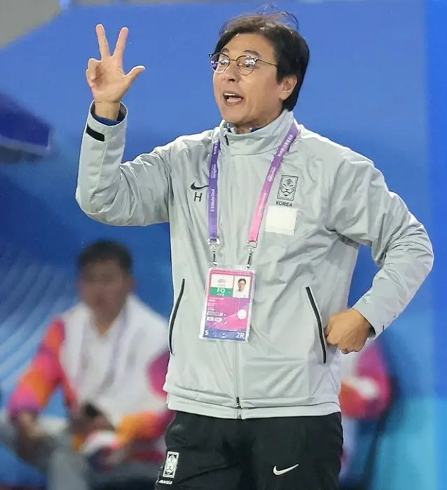 황선홍- 축구장 흰색점퍼 분홍색 목걸이 형 이름표를 목에걸고 오른손가락 3개를 펴며 소리지르고 있는 황선홍 감독