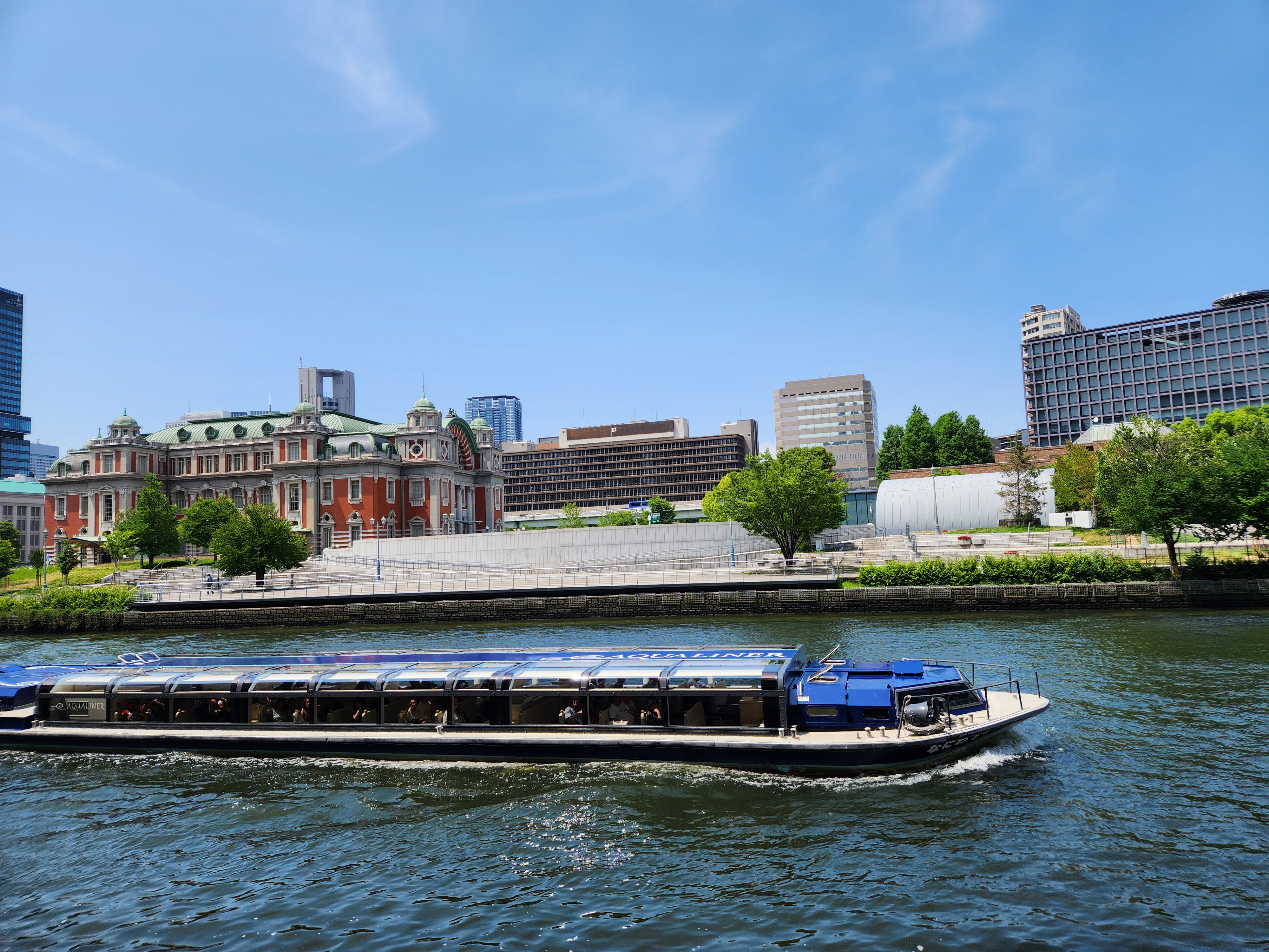 강 위를 천천히 지나가는 유람선과 오사카 중앙공회당이 보이는 강변 풍경