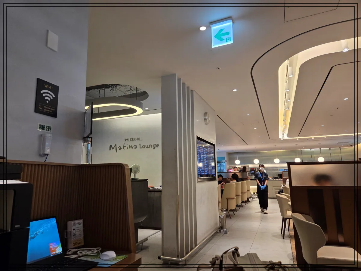인천공항-마티나-라운지-입구-앞-좌측에는-와이파이-안내판과-노트북이-있는-작업공간이-보이고-중앙에는-마티나-라운지-입구와-입장-대기줄이-형성된-좌석이-배치되어-있음-입구-상단에는-워커힐-마티나-라운지라고-적혀있고-안쪽에는-음식-코너와-라운지-직원이-서있는-모습이-보임