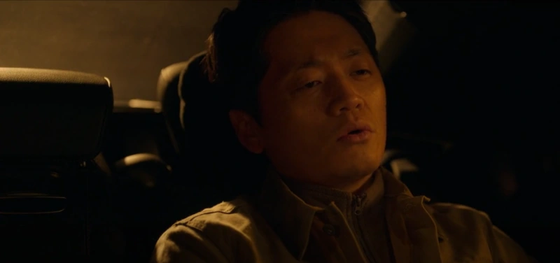 갈색 옷을 입고 승용자 뒷자석에 앉아 있는 드라마 무빙의 박찬일 캐릭터