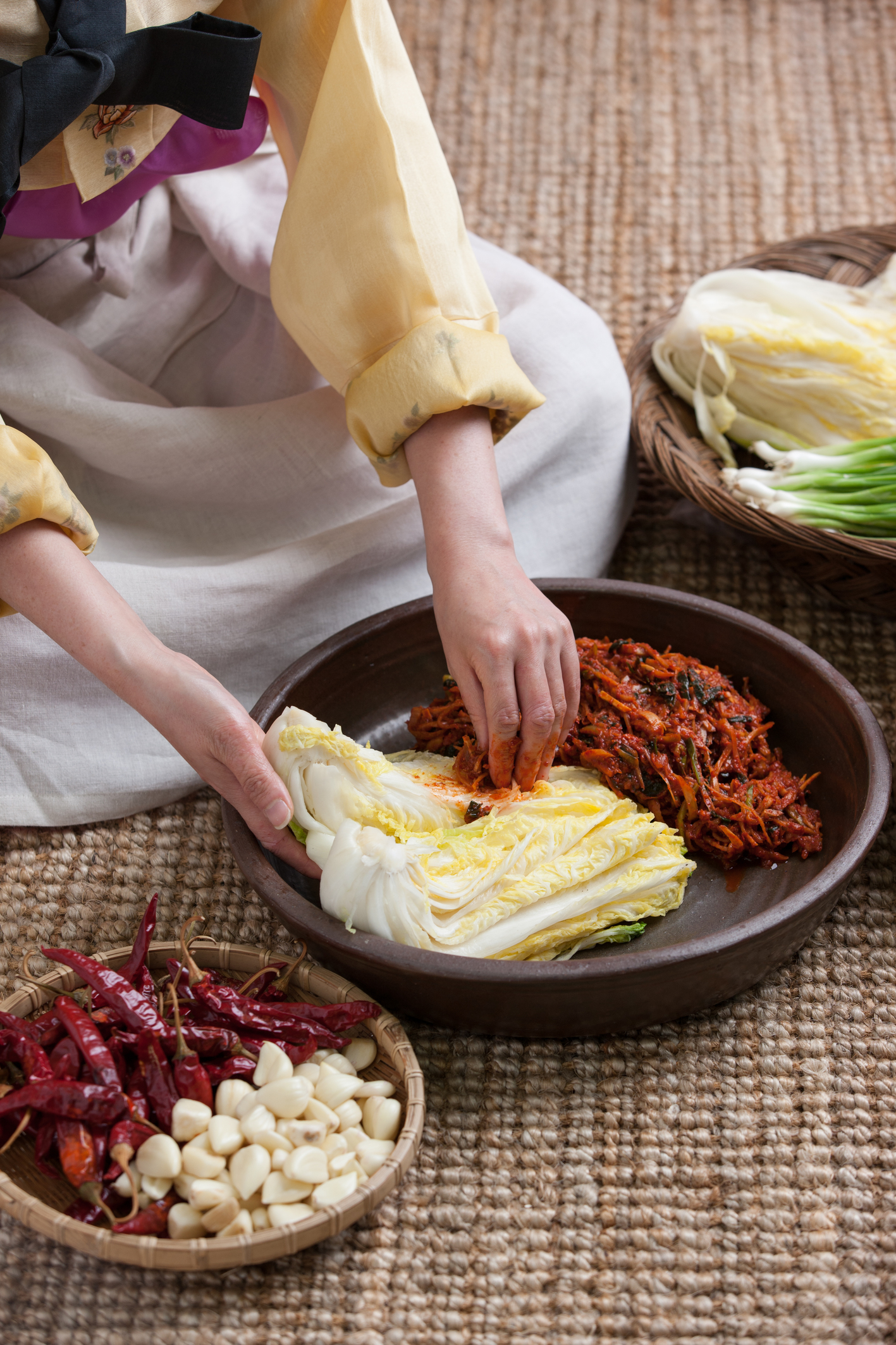 a woman in Hanbok sitting and making Kimchi