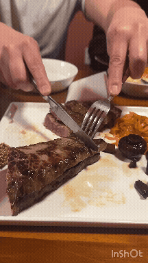 접시 위 스테이크를 포크와 나이프로 자르는 장면&amp;#44; 한쪽에 소스와 곁들임 메뉴가 함께 놓인 송년회 와인 모임 식사 장면