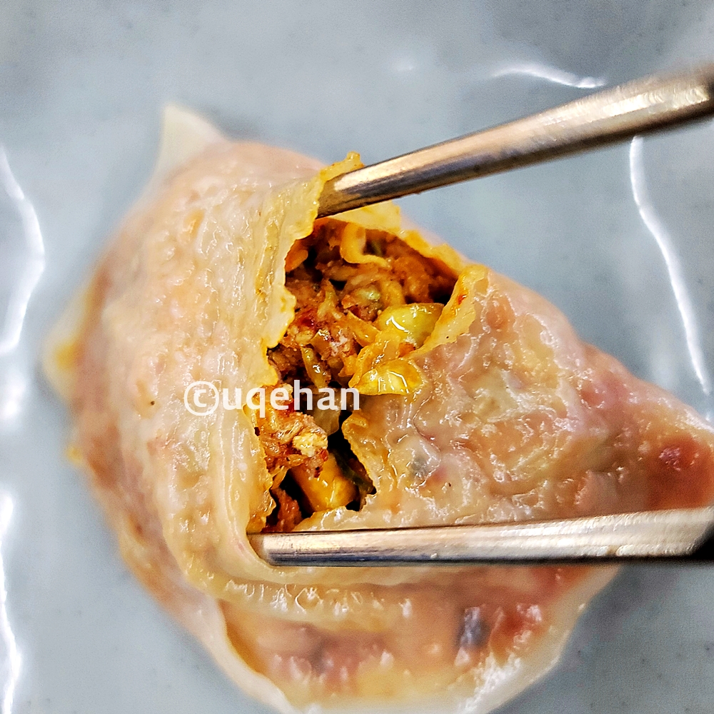 김치만두 1개를 젓가락으로 가운데부분의 만두피 부분을 벌려내고 있다.