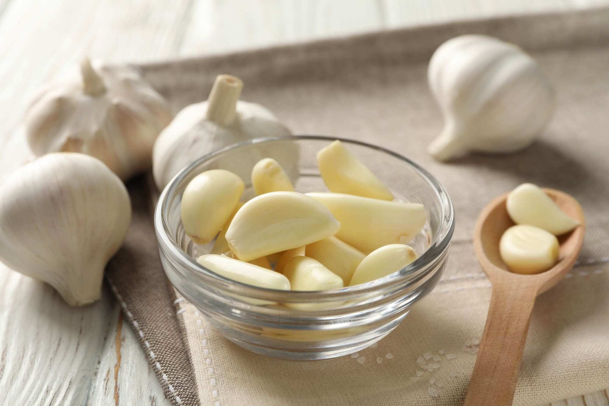 투명 유리볼에 담긴 생마늘, 통마늘과 나무 숟가락이 함께 놓인 모습