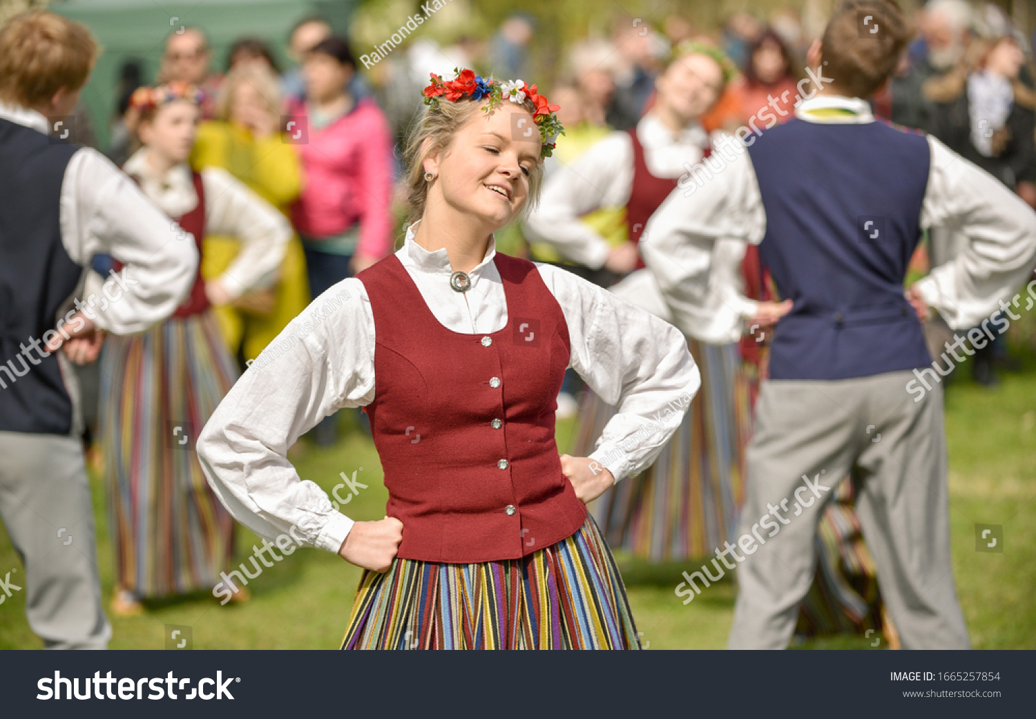 여러 사람의 남자와 여자가 정통의상을 입고 양손을 허리에 올리고 춤추는 사진입니다.