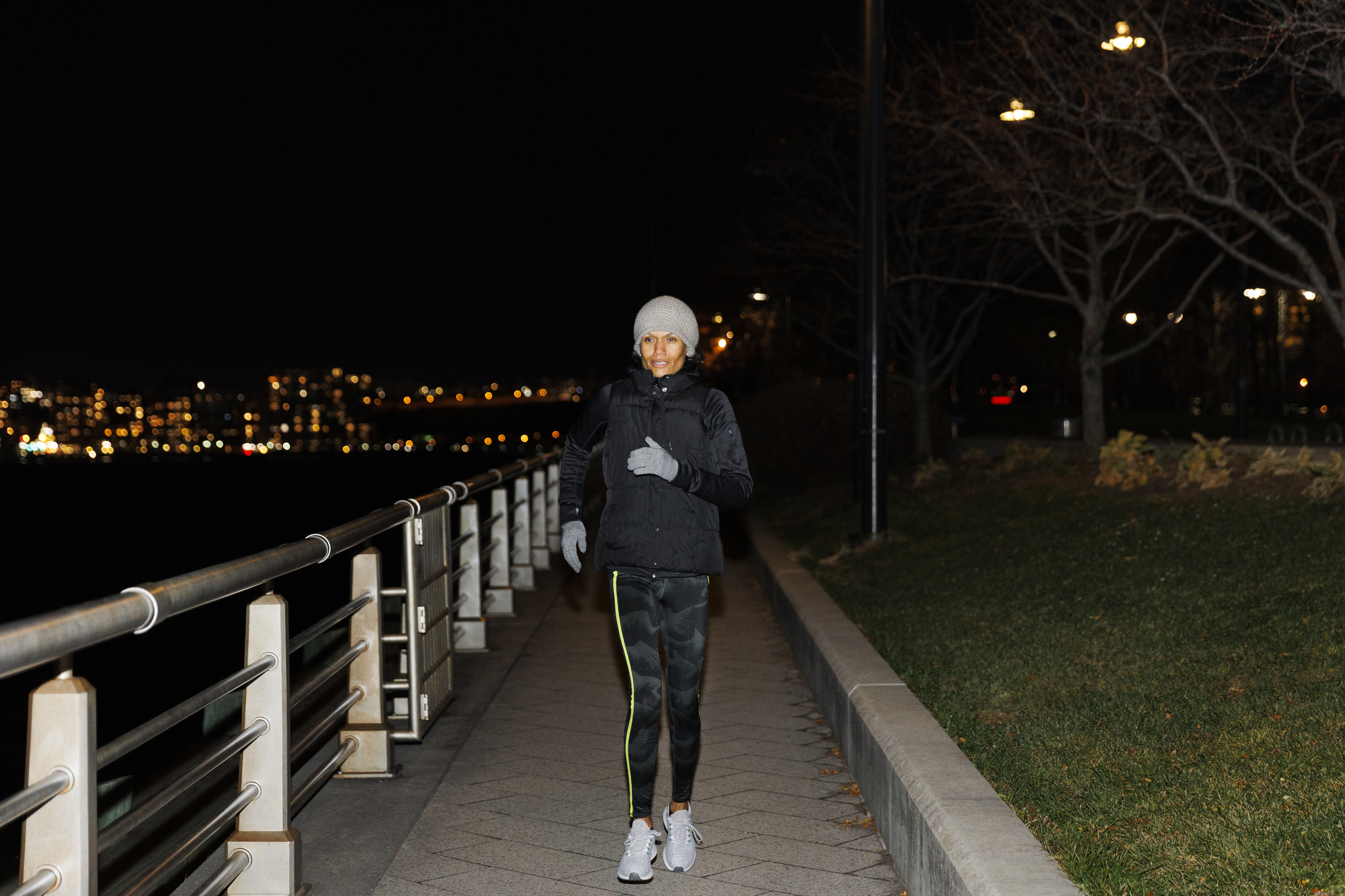 어두운 밤에 검은색 런닝복과 회색 모자와 장갑, 신발을 신은 여성이 혼자서 런닝을 하고 있는 사진