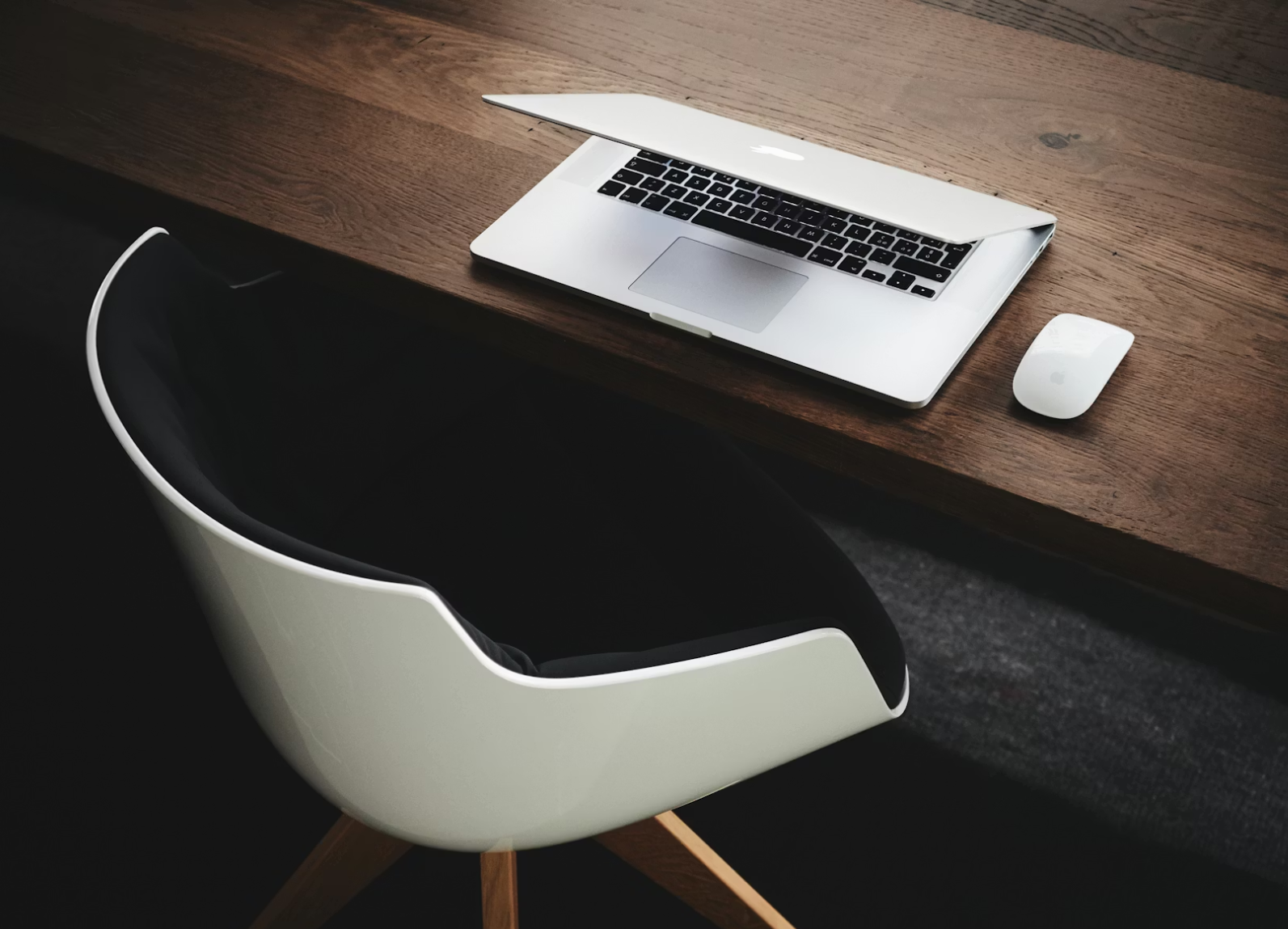 부분적으로 닫힌 노트북과 무선 마우스가 놓인 깔끔한 책상 위의 장면