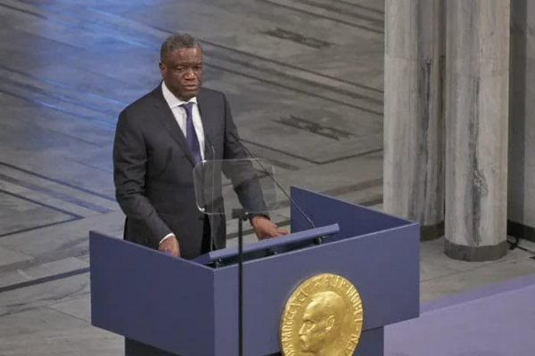 노벨상 표식이 있는 단상에 검은 정장 차림의 의사 무쿼게가 수상 기념 연설을 하는 모습