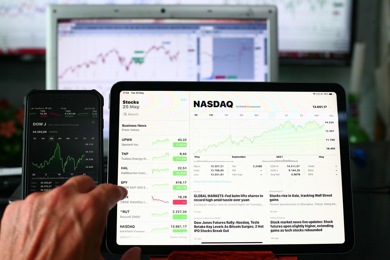 스마트폰과 태블릿 화면에 나스닥(NASDAQ) 지수와 주식 차트가 표시된 투자 관련 화면을 확인하는 모습