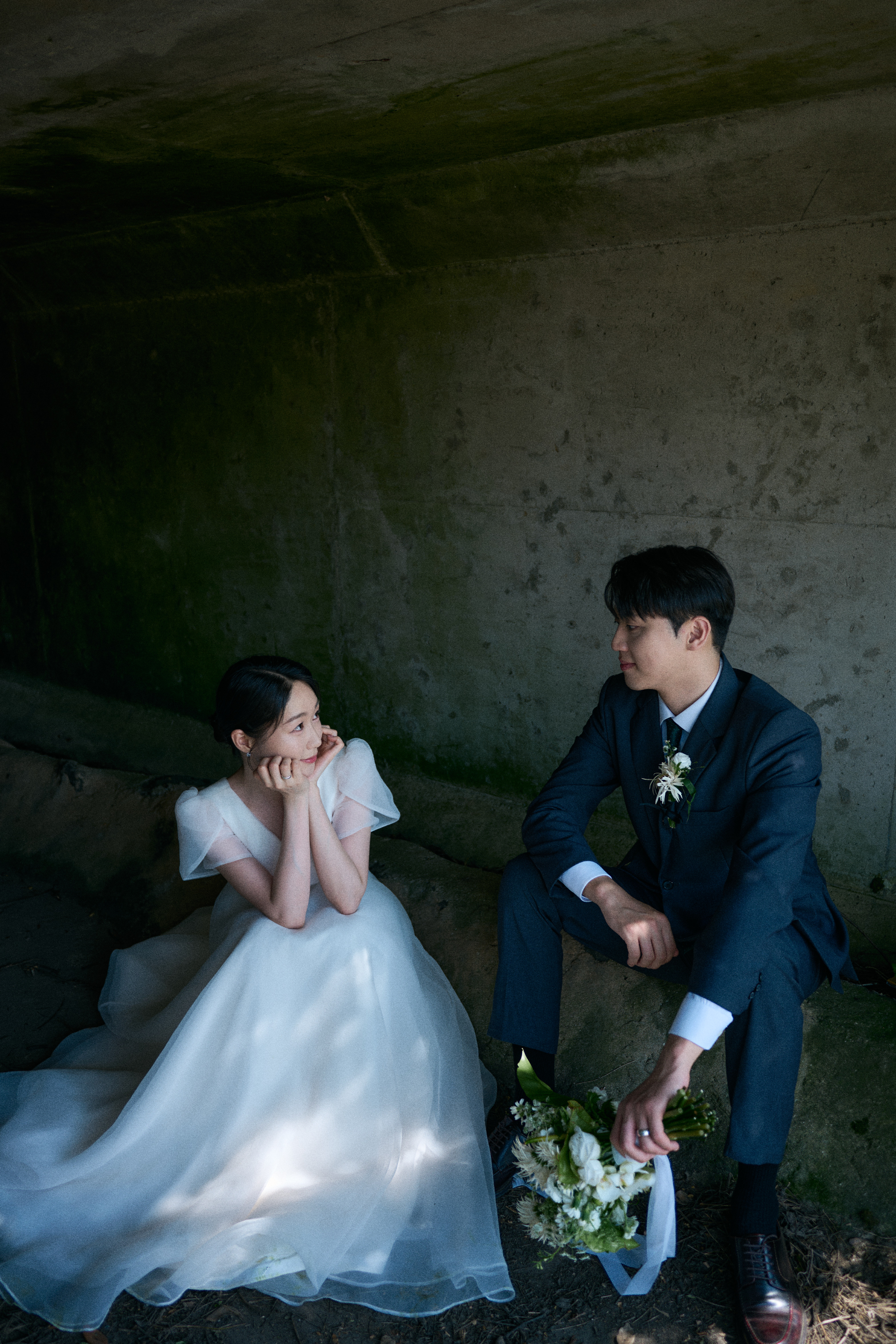 어두운 배경 속에서 서로를 바라보는 차분한 분위기의 제주 굴다리 웨딩 스냅