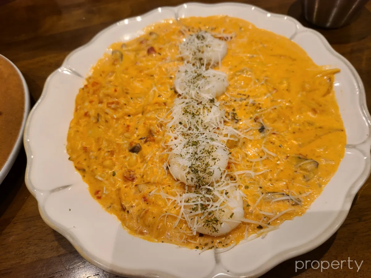 흰색굴곡있는테두리의접시-주황색소스가있는리조또-한줄로통새우5마리가있고-치즈와파슬리가뿌려져있다