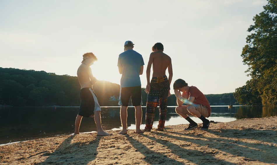 해변에서 노을을 바라보며 함께 시간을 보내는 네 명의 젊은 남성들