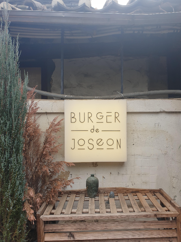 마당 한쪽 담에 버거 드 조선이라고 쓰인 조명 간판이 부착되어 있다.
