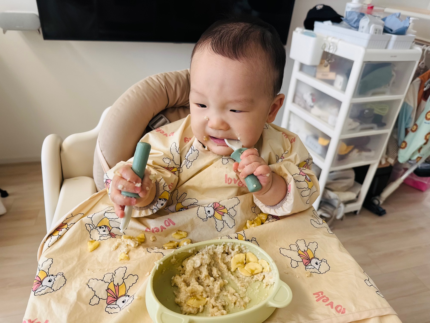 약간 찡그린 얼굴로 포리지를 먹으며 양손에 식기를 쥔 9개월 아기 찬솔이의 귀여운 모습