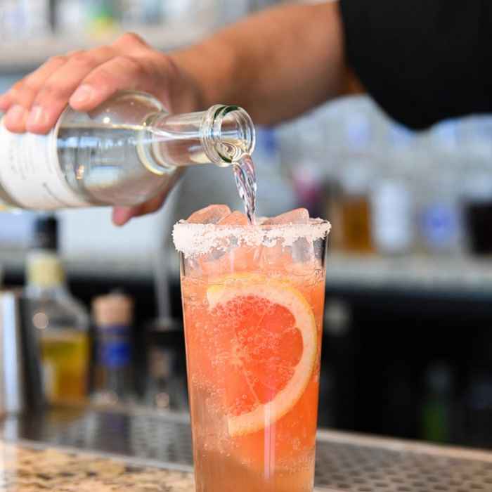 솔트 리밍된 잔에 자몽 소다를 부어 기포가 올라오는 메스칼 팔로마 제조 장면