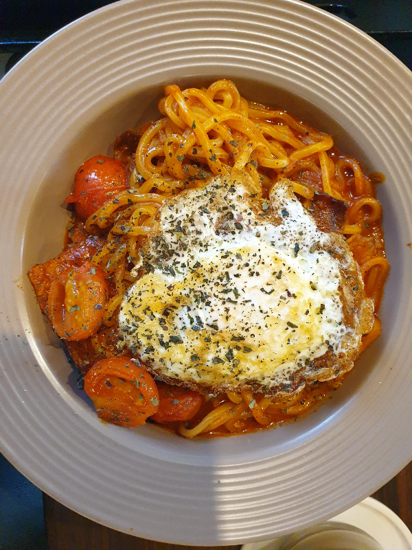 계란이 올려져 있는 라볶이. 방울 토마토와 파슬리 가루도 보인다.