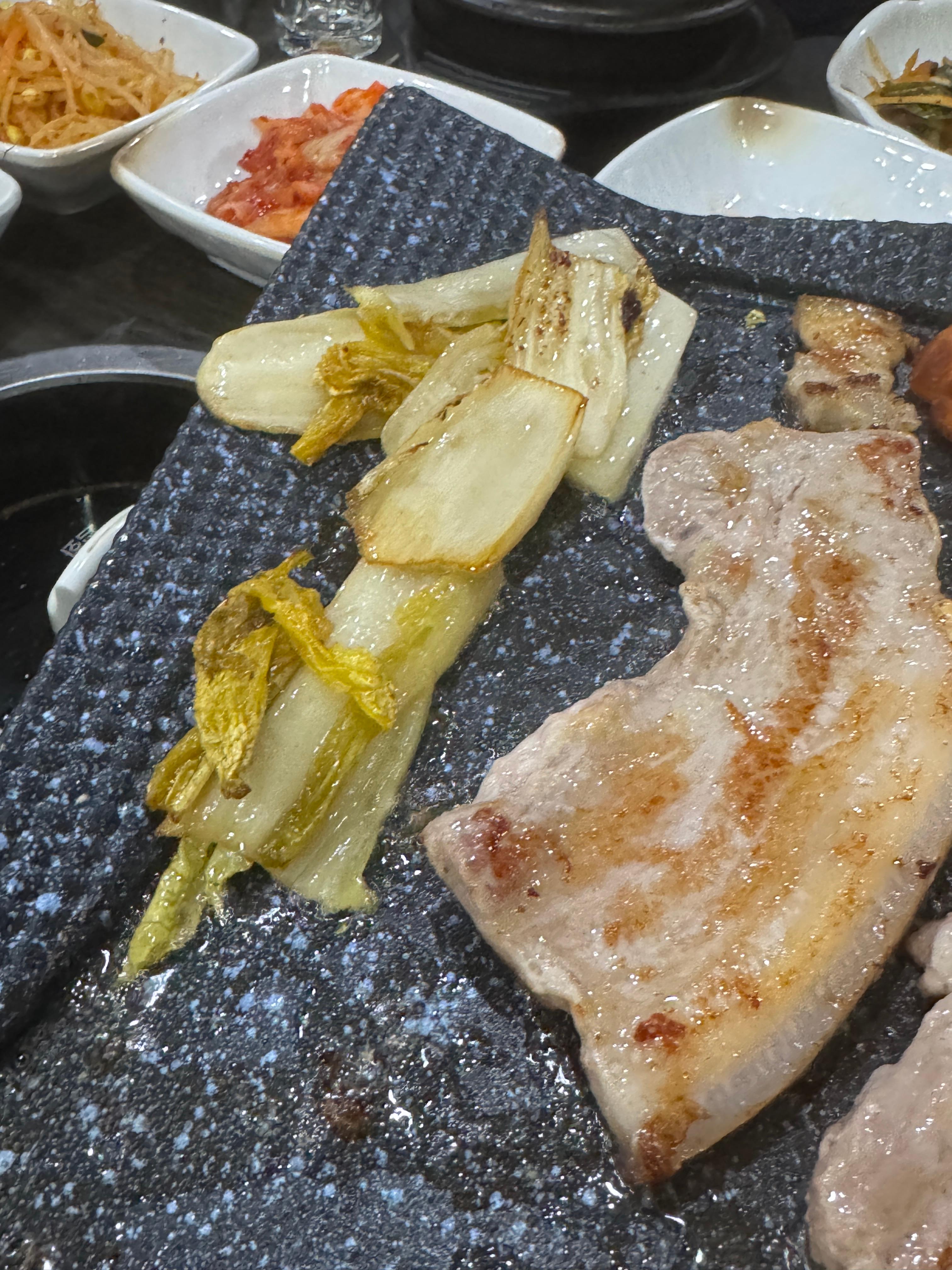 불판 위에서 제주산 오겹살과 백김치가 함께 구워지고 있는 장면.