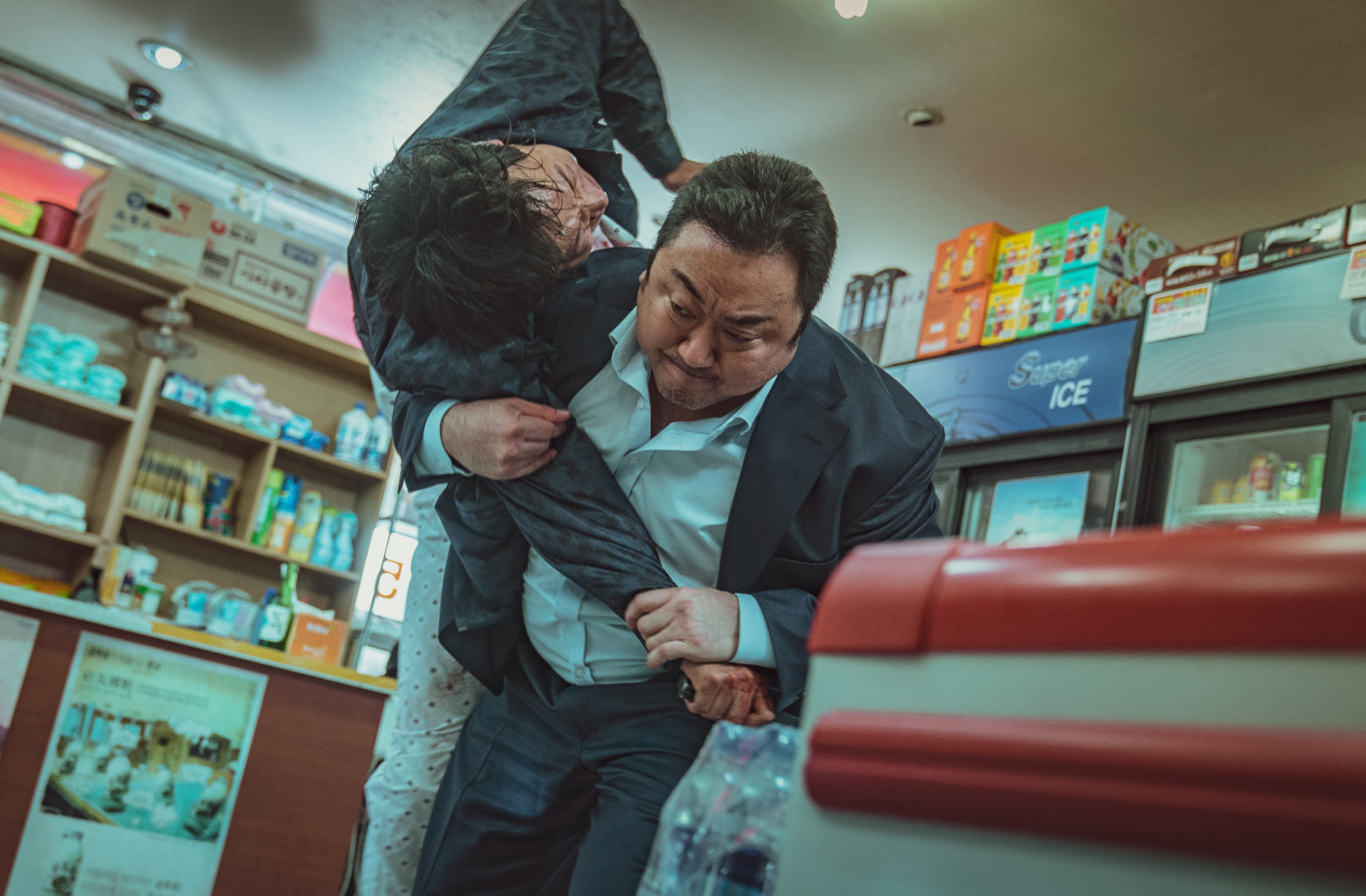 편의점 안에서 마석도가 상대를 붙잡아 제압하는 격투 장면, 좁은 실내 공간에서 박진감 넘치게 전개된다