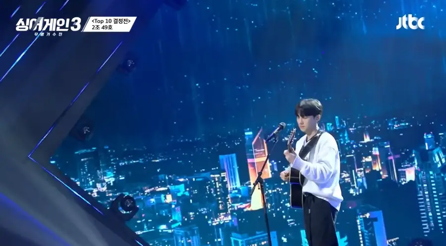 싱어게인3 - 흰색 티를 입고 스탠딩 마이크 앞에서 기타를 두손으로 치는 49호