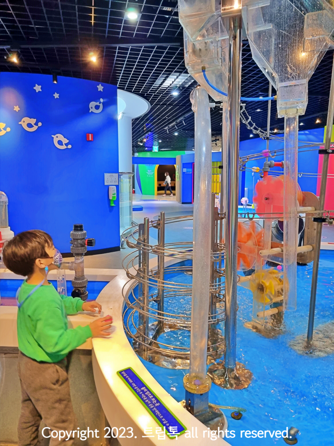 물 안에 여러가지 기구들이 설치 되어서 공이 내려오는데 그 모습을 아이가 보고 있다.
