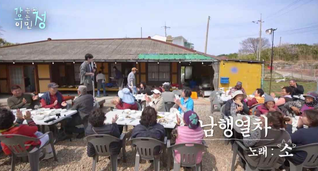 마을 주민들 사이의 평상에 김정현이 올라가서 남행열차를 부르는 장면에 남행열차 노래 소 라는 자막이 있는 스틸컷