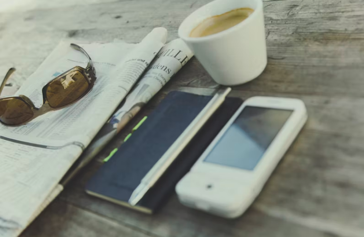 테이블 위에 놓인 종이 신문, 스마트폰, 노트, 커피잔