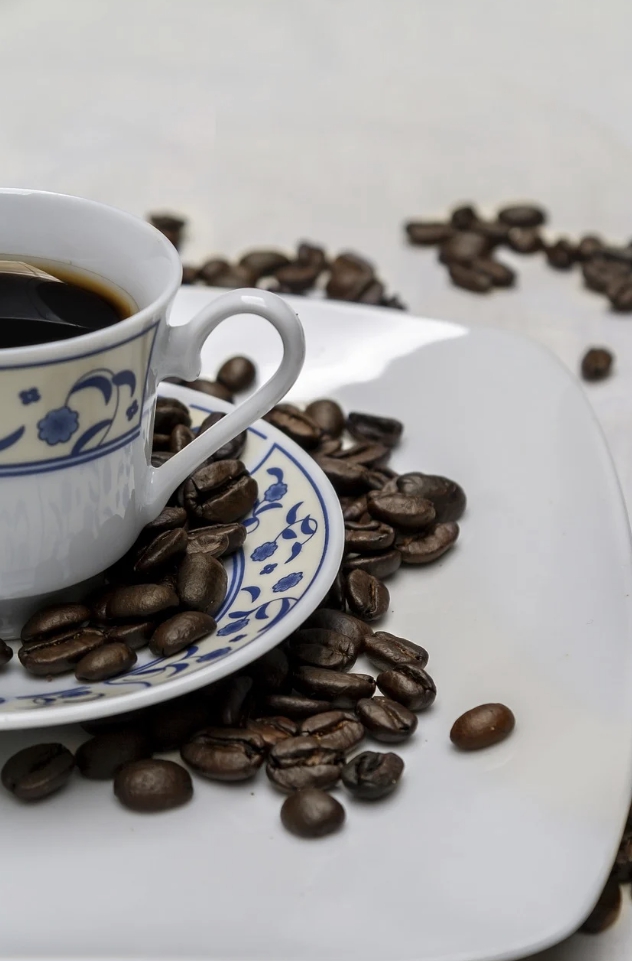 커피잔에 담긴 커피와 그 주면의 커피콩 사진