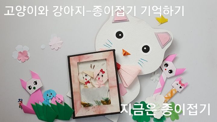 강아지 액자와 고양이를 한 곳에 놓았어요. 옆에는 작은 강아지 접기세 마리가 풀밭에 앉아 있고, 막대 접기에 고양이 얼굴을 붙인 막대 인형 두 개가 있어요.