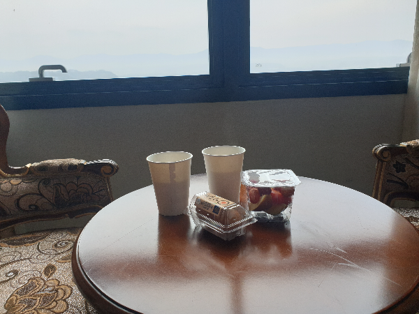 창가 바로 앞에 테이블이 있고, 테이블 위에는 컵 2개와 계란 그리고 과일이 있다.