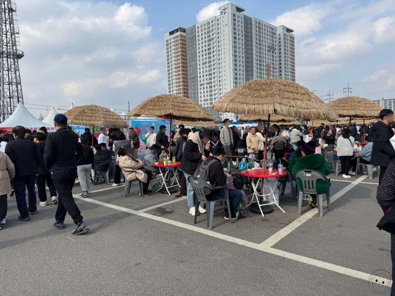 야외 행사장에서 많은 사람들이 테이블에 앉아 식사하는 모습.