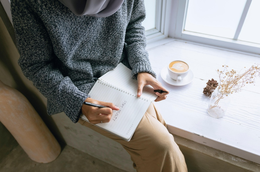 노트에 'STAY HEALTHY'를 적으며 건강 습관을 기록하는 여성의 모습 - 습관 형성과 유지 전략에 관한 심리학적 접근