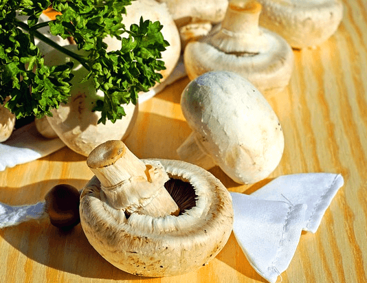 나무 도마에 하얀 양송이버섯들이 가득하다. 작고 앙증맞게 생겼고, 왼쪽엔 초록색 파슬리가 있다.