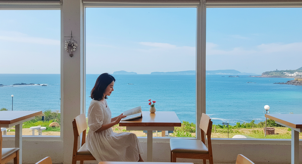 제주 오션뷰 카페에서 책을 읽으며 여유를 즐기는 한국인 여성