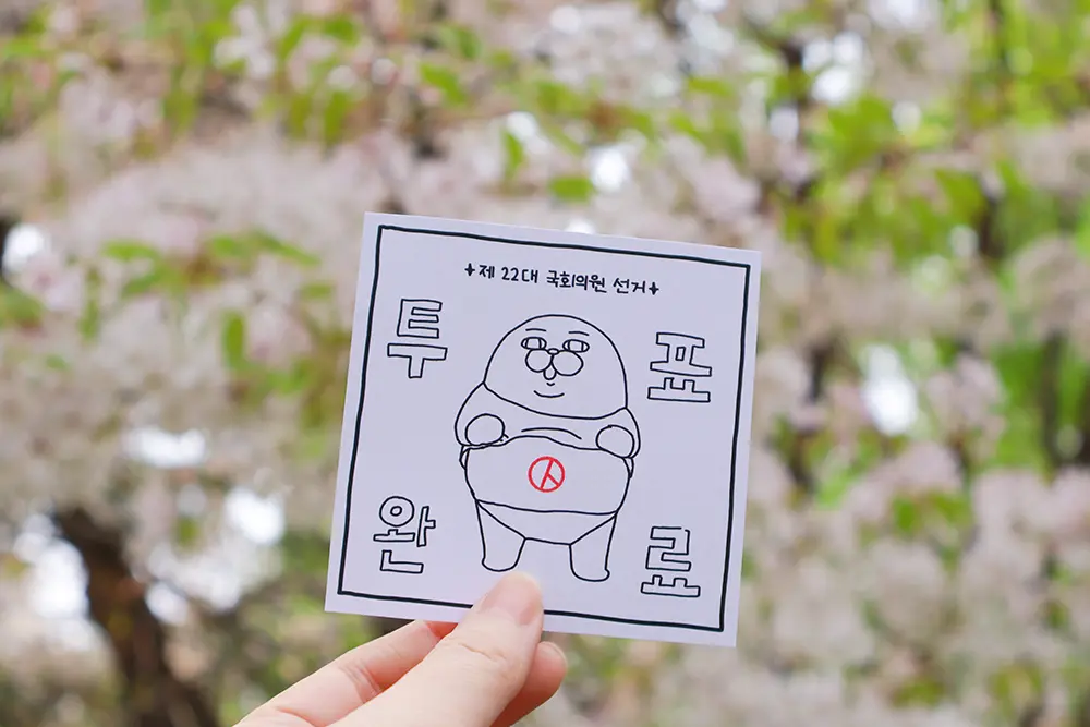 벚꽃-배경으로-투표-인증-종이-들고-있는-손