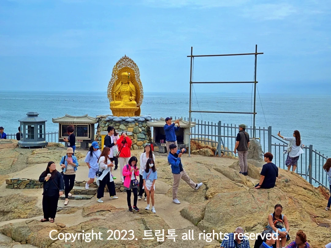 노란생 불상이 바다를 배경으로 있고 그 아래 바위에 많은 사람들이 있다