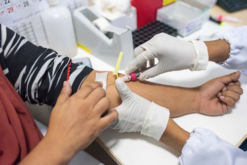 대장암 검진 분변잠혈검사 비용 주기 준비사항 관련 참고 이미지: 의료 전문가가 흰색 장갑을 착용하고 환자의 팔에서 혈액 샘플을 채취하는 장면. 채혈 튜브에 혈액을 수집하고 