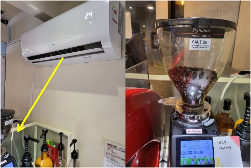 카페 주방 벽면에 설치된 하얀색 에어컨의 찬 바람이 아래쪽에 위치한 Dynamic 원두 그라인더 호퍼 방향으로 향하고 있는 모습을 노란색 화살표와 점선으로 강조한 사진. 에어컨 바람에 의한 미세한 온도 변화가 원두 분쇄도를 흔들어 추출 시간을 춤추게 만드는 '역설적 상황'과 이를 잡기 위한 사장의 보이지 않는 사투를 논리적으로 설명함.