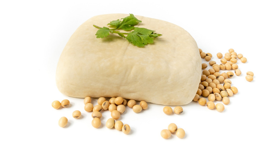 하얀 바닥 위에 두부콩으로 만든 두부를 중앙에 놓고, 그 위에는 풀잎으로 장식을 해 놨고, 두부 주변에 두부콩을 흩어놓고 찍은 사진