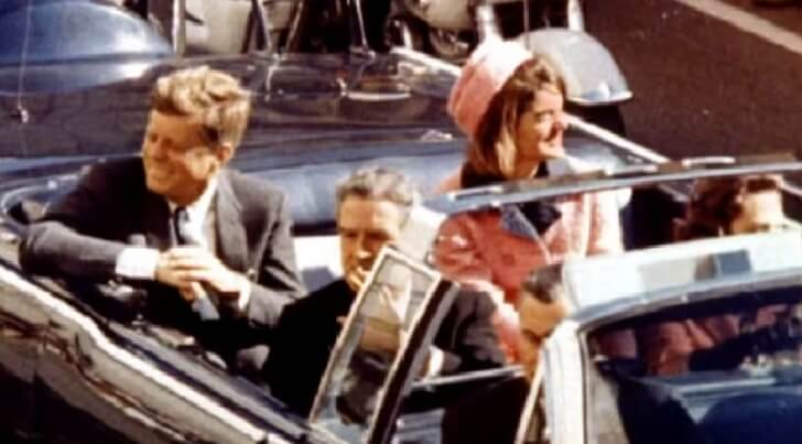 차량을 타고 이동 중인 미소를 띤 존 F 케네디