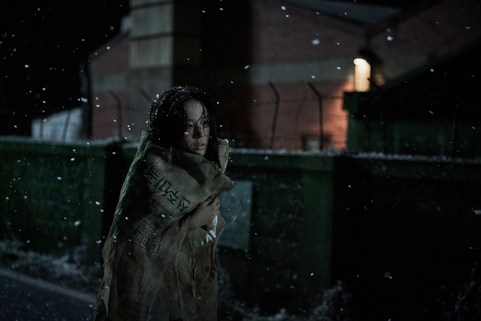 한 여성이 눈이오는 밤 길을 도망가고 있다.