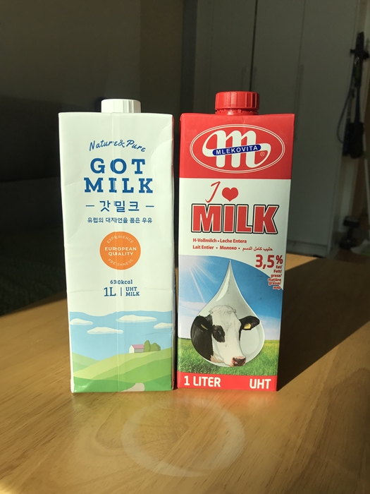 수입 멸균 우유 갓밀크와 믈레코비타 아이러브밀크 패키지 비교 사진. 갓밀크는 흰색 배경에 목초지 일러스트가 그려져 있고, 믈레코비타는 붉은색 포장과 젖소 일러스트가 특징이다.