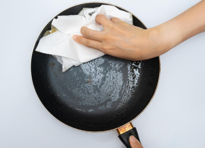 프라이팬의 기름때를 키친타월로 닦고 있는 손의 모습