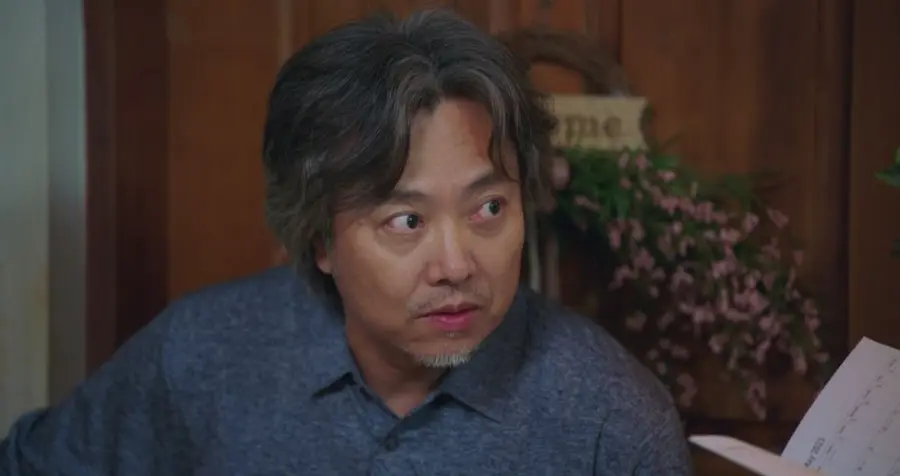 웰컴투삼달리- 파란셔츠에 머리가 히끗히끗한 아저씨가 눈을 동그랗게 뜨고 상대방을 궁금하게 쳐다보는 모습