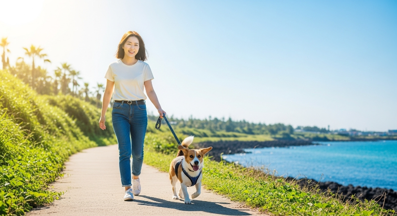 제주 해안 산책로에서 반려견과 즐겁게 산책하는 30대 여성의 활기찬 모습.