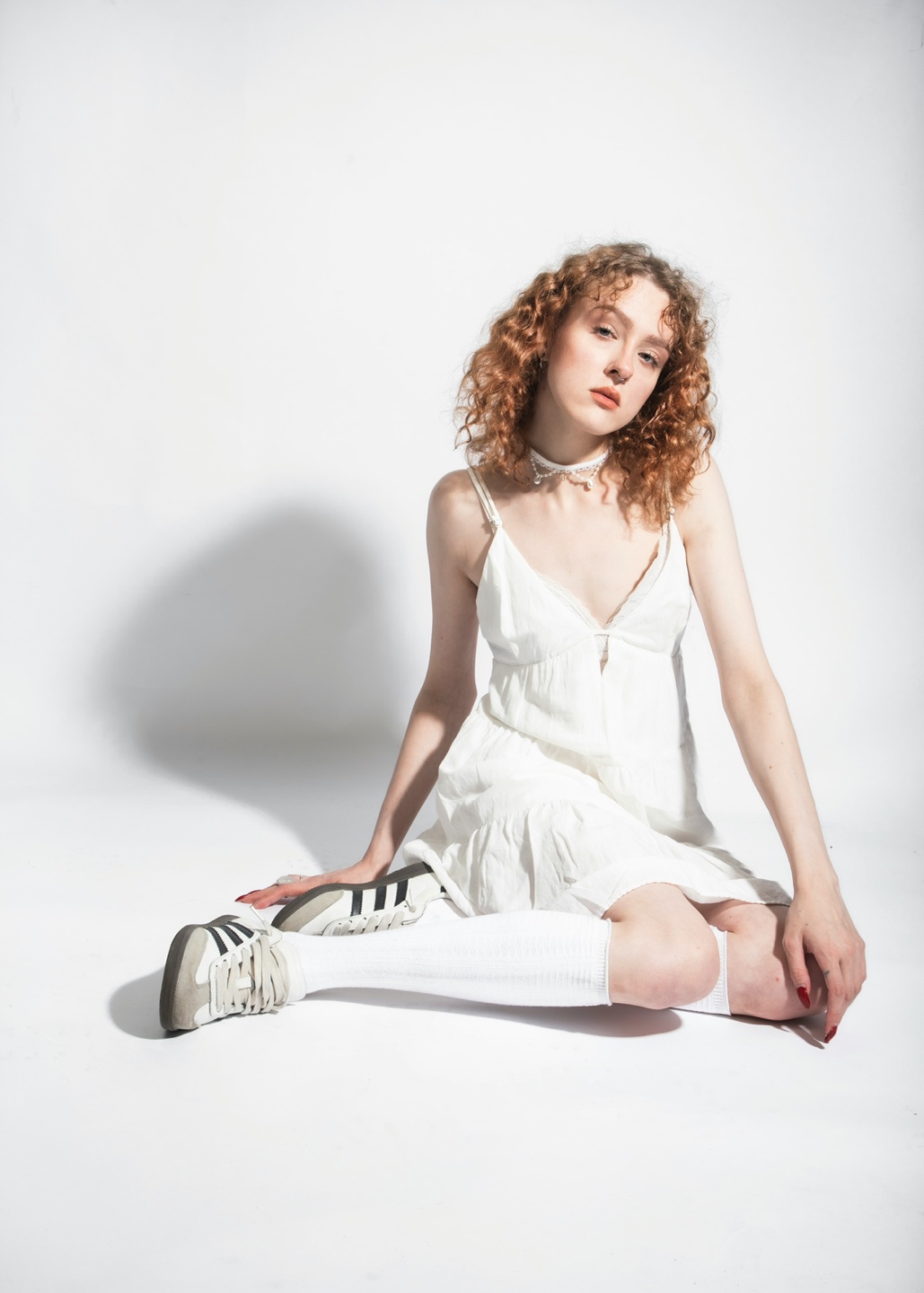 흰색 원피스를 입고 아디다스 스니커즈를 입고 앉아있는 여성 사진